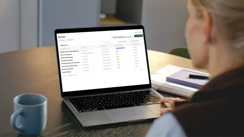 A person at a laptop viewing the All Records list for their home, with each uploaded document's file name, record type, and date