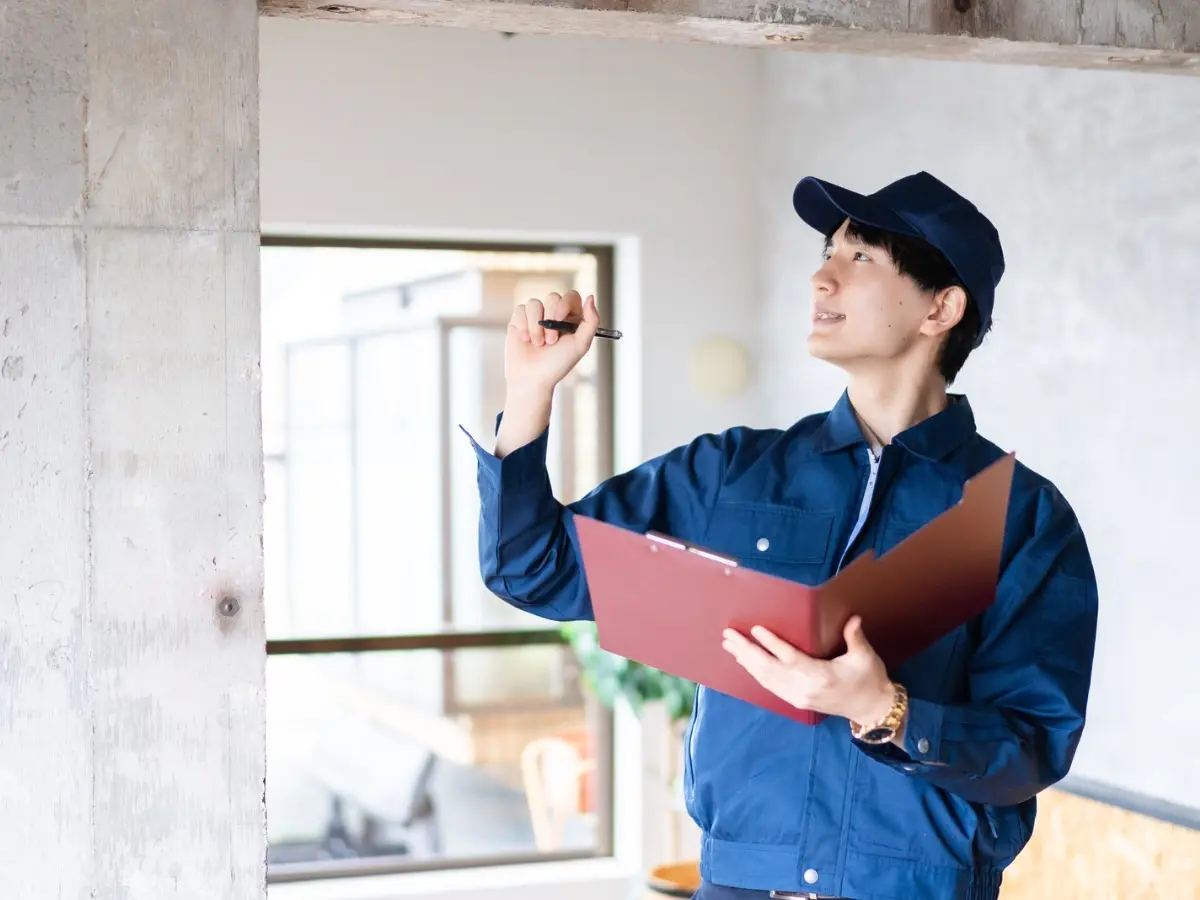 A home inspector holding a clipboard, looking up at the ceiling framing during a walkthrough