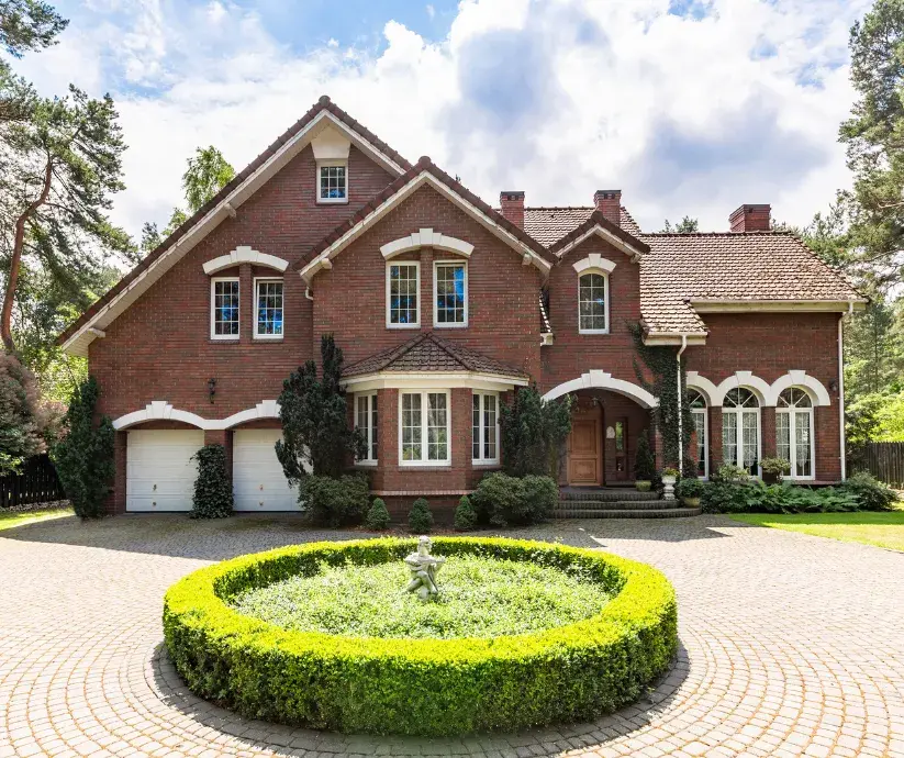 A large brick house with an arched entrance, a circular garden, and a paved driveway