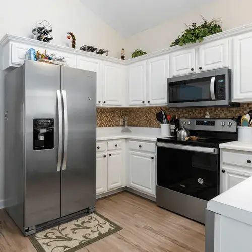 Kitchen in a home with white cabinets, a stainless steel refrigerator, a range with a kettle on it, and an over-range microwave.